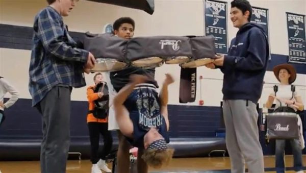 Senior tenor drummer Ben Herring keeps the beat while hanging upside down, supported by fellow section members (from left) Dane Fordahl, Jonathan Ford and Bassel Daniel, during a lunchtime Drumline performance to celebrate Spirit Week, held in the Main Gym on Thursday, Oct. 19, 2023. 